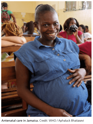 Summary : This photograph shows a pregnant woman seated in a waiting area, likely a clinic or healthcare facility, with other women in the background, illustrating the context of antenatal care in Jamaica.
photo:
Scene Overview :
• Main subject is a visibly pregnant woman sitting on a wooden bench, wearing a blue button-up dress.
• The setting appears to be a clinic or healthcare waiting room, with several other women seated on benches in the background.
• The perspective is at eye level, focusing on the woman in the foreground.
• Lighting is natural or fluorescent, typical of indoor public health facilities.
• The colour palette includes neutral tones, with the blue dress of the main subject standing out.
Technical Details :
• No scale bar or magnification is present.
• No visible on-image text or user interface elements.
• The image is credited to WHO / Aphaluck Bhatiasevi.
Spatial Relationships :
• The pregnant woman occupies the foreground, positioned centrally and slightly to the right.
• Other women are seated behind her, some facing forward, others turned to the side, indicating a communal waiting area.
• The benches are arranged in rows, suggesting an orderly seating arrangement.
Analysis :
• The image visually communicates the experience of antenatal care in Jamaica, highlighting the communal aspect of healthcare access for pregnant women.
• The focus on the pregnant woman in the foreground draws attention to maternal health as a central theme.
• The presence of multiple women in the background suggests a shared healthcare environment, possibly indicating demand for antenatal services.