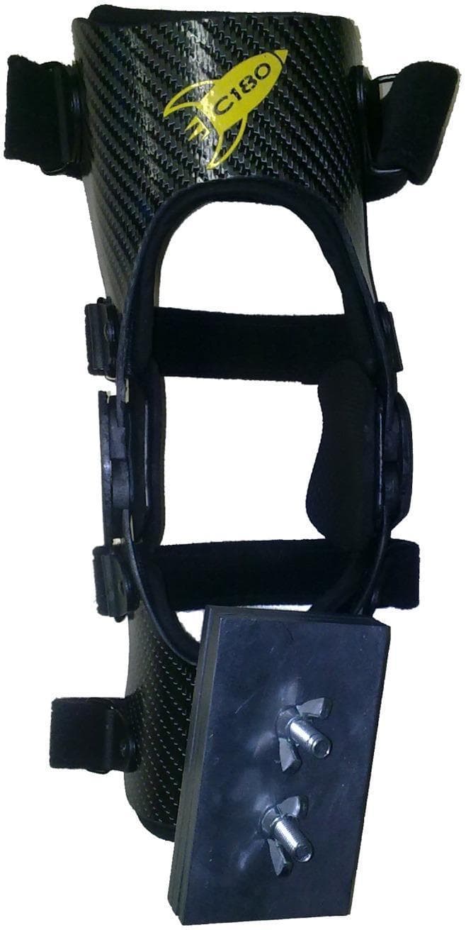 A clinical photograph of an orthopedic medical device, specifically a modified rigid knee-stabilizing brace used in rehabilitative research. The brace features a carbon-fiber textured frame with a contoured anatomical design, incorporating a circular patellar opening and articulated bilateral hinges to allow controlled flexion and extension. It is secured via multiple adjustable hook-and-loop (Velcro) straps positioned at the thigh and calf sections to ensure customized compression and stabilization. A unique modification for gait analysis or strength training is visible at the distal (lower) anterior portion, where a rectangular black lead mass is externally affixed using two metal bolts and wingnuts. This setup is clinically relevant for studies involving gait kinematics in populations such as children with cerebral palsy, where added resistance or weight on the proximal third of the leg is used to evaluate changes in joint rotation and motor control.