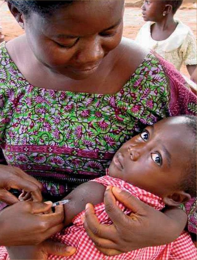 This clinical photograph captures a pediatric vaccination procedure in a global health setting. A healthcare provider is shown administering an intramuscular or subcutaneous injection into the deltoid region of an infant's upper left arm. The equipment visible is a small-gauge syringe with a fine-bore needle, consistent with standard immunization protocols. The infant is cradled securely by a caregiver, who is observing the procedure. This visual illustrates key concepts in public health, including routine childhood immunization programs, primary care delivery in developing regions, and efforts to reduce under-five mortality. The focus of the image is on the precision of the injection technique and the delivery of preventative medicine. Relevant medical themes include maternal and child health (MCH), immunology, and community-based healthcare interventions.