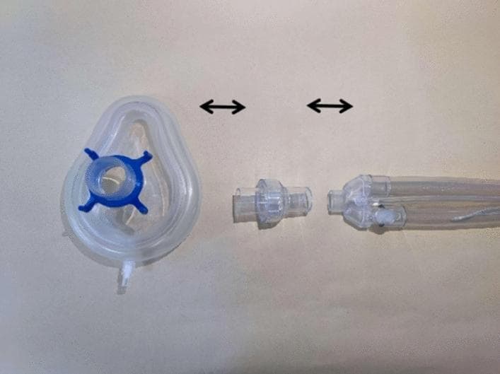 This clinical photograph serves as a schematic diagram illustrating the assembly of a non-invasive high-frequency oscillatory ventilation (NIHFOV) circuit. The image displays three primary medical device components arranged horizontally on a neutral background, with double-ended black arrows indicating the connection sequence. From left to right, the components include: 1) A clear, teardrop-shaped silicone non-invasive ventilation (NIV) mask featuring a blue four-pronged headgear attachment ring and a distal sampling port. 2) A clear, cylindrical disposable leak valve designed to facilitate the venting of exhaled CO2. 3) A proximal segment of a flexible, transparent ventilator breathing circuit showing multi-lumen tubing. The setup demonstrates the critical interface between the ventilator tubing, the mandatory leak valve for safety and gas exchange, and the patient interface (mask). This visual is intended for clinical training and educational instruction on the proper configuration of NIHFOV hardware for respiratory support.