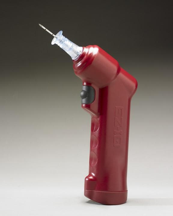 A clinical photograph of the EZ-IO® battery-powered intraosseous (IO) vascular access driver. The device is a handheld, ergonomic power driver featuring a burgundy or dark red plastic casing with molded finger grips and the 'EZ-IO' logo embossed on the handle. A black trigger switch is positioned on the inner neck of the handle for activation. At the distal end, a clear plastic hub is attached, which secures a 15-gauge stainless steel needle (cannula). The needle tip is beveled, designed for piercing cortical bone to establish rapid vascular access in emergency or critical care settings. This device is used when intravenous (IV) access is difficult or impossible, allowing for the infusion of fluids and medications directly into the bone marrow cavity. It is a critical tool in emergency medicine, trauma, and resuscitation, providing a reliable alternative to central venous catheterization with a faster insertion time.