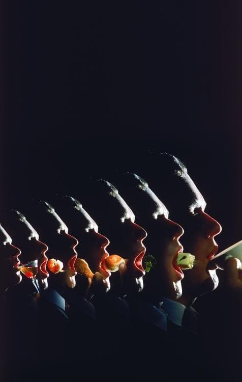 An educational infographic and clinical conceptual image illustrating the relationship between dietary diversity and the human microbiome. The image features a sequential progression of human silhouettes in profile, each with an open mouth receiving a different dietary item. The food sequence includes a cocktail with a garnish, a shrimp, a fried protein, a carbohydrate-rich bun, a floret of broccoli (representing high-fiber vegetable intake), and a cube of cheese. This visual composition serves as a metaphorical representation of the diverse environmental exposures introduced through diet. Centrally, the image focuses on how individual dietary choices serve as the primary substrate for intestinal bacteria. Clinically, it illustrates concepts related to gastroenterology, nutrition, and personalized medicine, highlighting how variations in the gut microbiome may influence individual susceptibility to environmentally-induced diseases through the differential metabolism and bioavailability of ingested compounds.