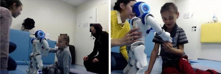 Two side-by-side clinical photographs illustrating a Socially Assistive Robot (SAR) intervention within a neurodevelopmental rehabilitation setting, likely for Autism Spectrum Disorder (ASD). The images demonstrate the experimental setup in a controlled environment featuring padded sports mats on the floors and walls for safety. The left panel shows a child sitting on the floor interacting with a blue and white humanoid robot while an adult (parent or therapist) observes closely. The right panel captures a more direct tactile interaction where the child touches the robot's arm, and the adult provides physical guidance or support. The setup is designed to evaluate social engagement, joint attention, and behavioral responses (such as chest-button pressing or verbalization) in pediatric patients during robot-mediated therapy. The presence of cameras on the walls indicates a recorded session for quantitative behavioral analysis, such as ADOS-2 scoring or engagement metrics. This clinical scenario highlights the use of assistive technology in therapeutic interventions to facilitate social communication and reduce aggressive behaviors in verbal and non-verbal children.