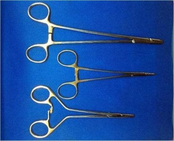 A clinical photograph of three different surgical needle holders used in specialized suturing procedures, displayed against a blue surgical drape. All three instruments are made of stainless steel with a metallic finish and feature ratcheted locking mechanisms and slender jaws designed for gripping suture needles. The top instrument is a 20.5 cm Stille Mayo-Hegar Needle Holder (LMH), a standard larger-format instrument for heavy tissue suturing. The middle instrument is a 16 cm Stille Mayo-Hegar Needle Holder (SMH), providing a more compact profile for refined manipulation. The bottom instrument is a 15 cm Stille Frimand Duo-Grip Needle Holder (FR), which distinguishes itself through a unique ergonomic handle design; it features offset finger rings and a curved lever arm leading to the ratchet, intended to enhance grip control and tactile feedback. These instruments represent various mechanical designs optimized for surgical anastomoses, where precise control over needle placement is critical.